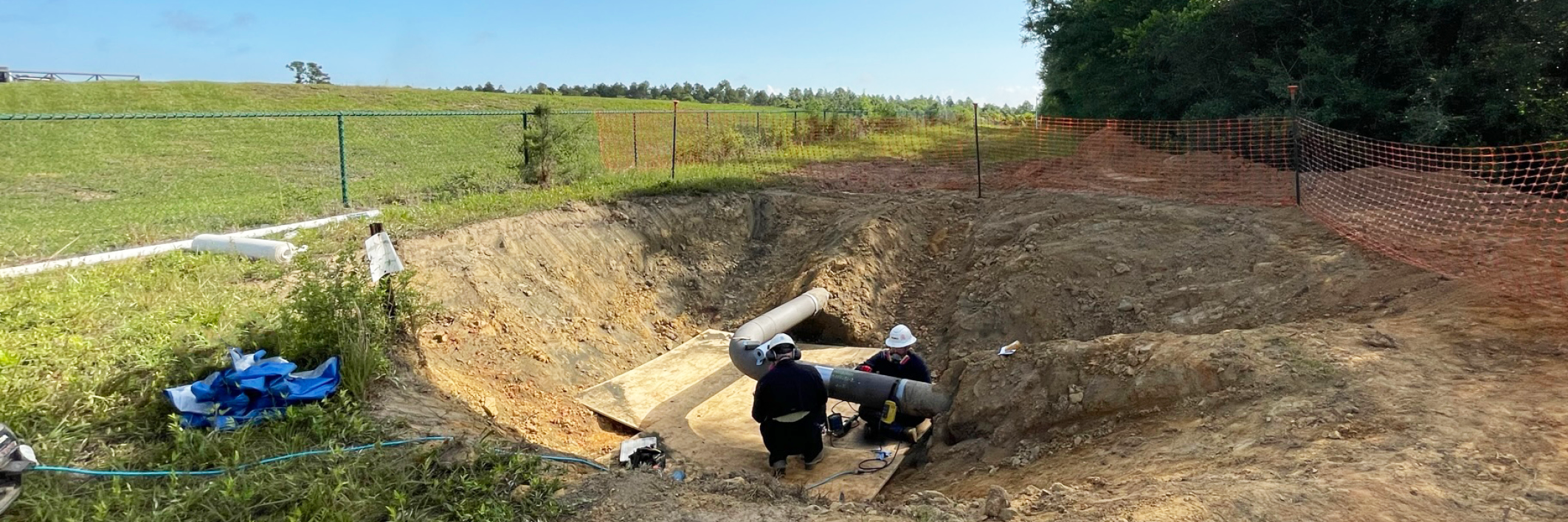 Two people inspecting an excavated pipeline.