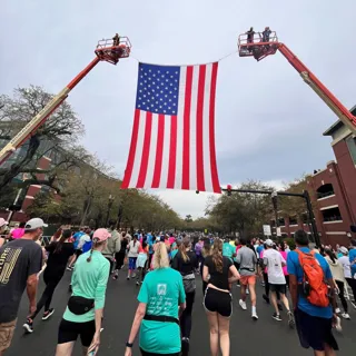 Crowd walking in a race in front of large American flag